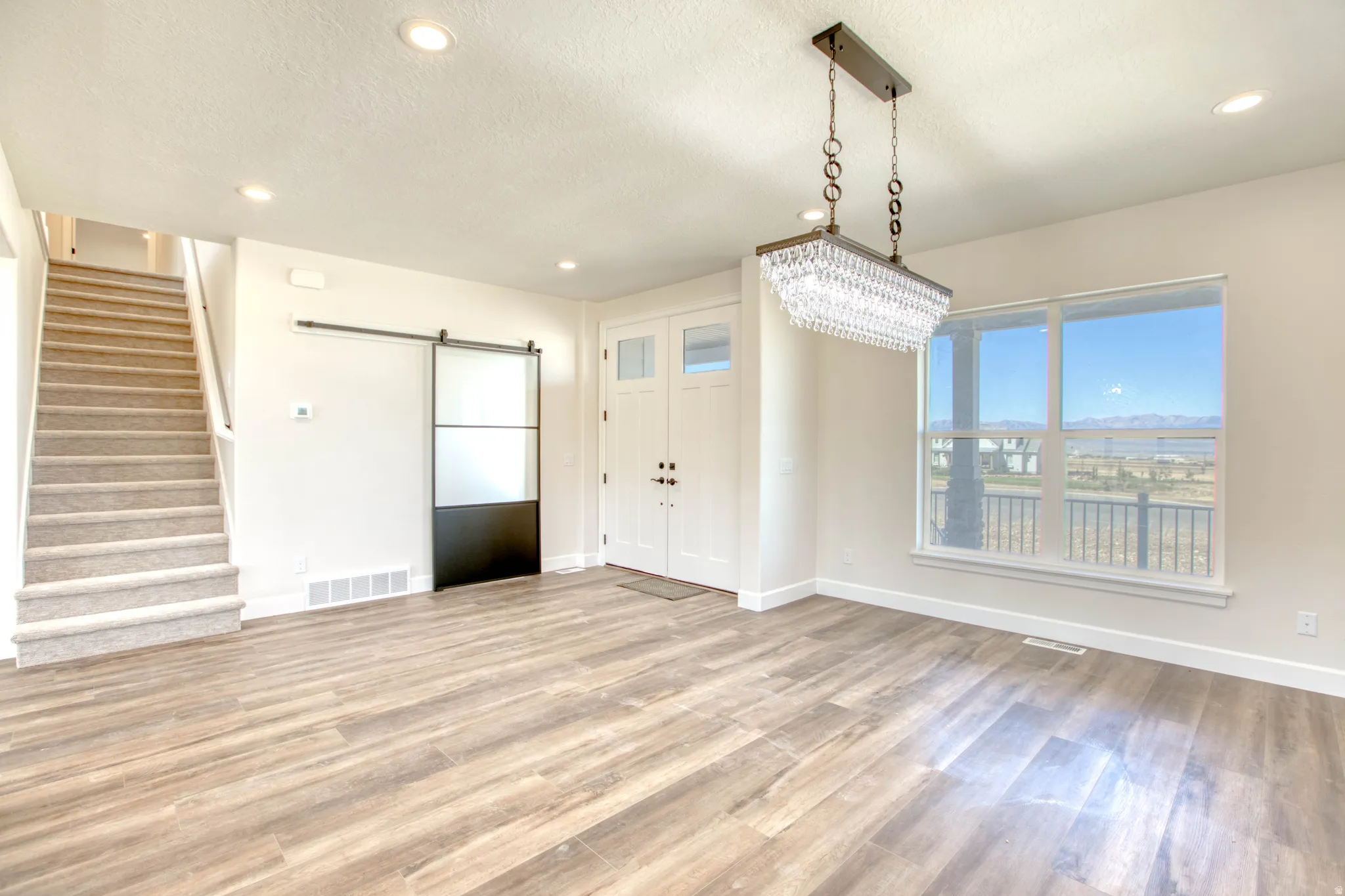Wood-finish flooring, recessed ceiling lighting, a crystal chandelier, a two-panel front entry door, and an interior barn door