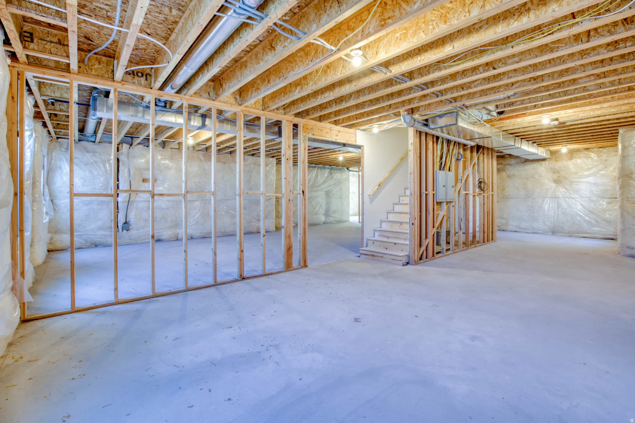 Unfinished basement with exposed wood framing, concrete flooring, and an unfinished staircase