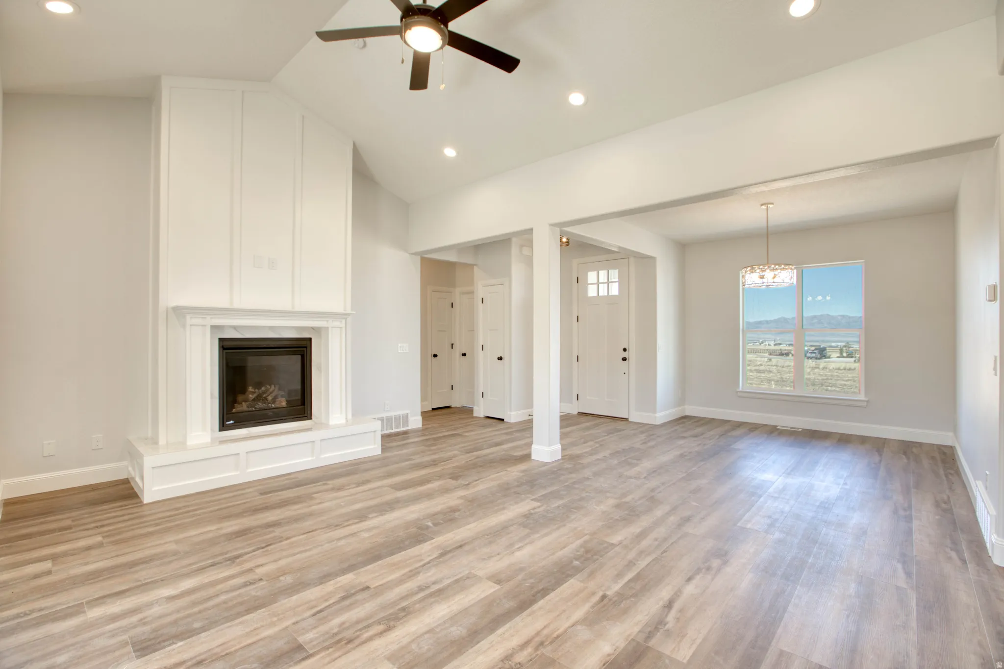 Vaulted ceiling with recessed lighting, wood-finish flooring, and a fireplace with a white mantel and hearth