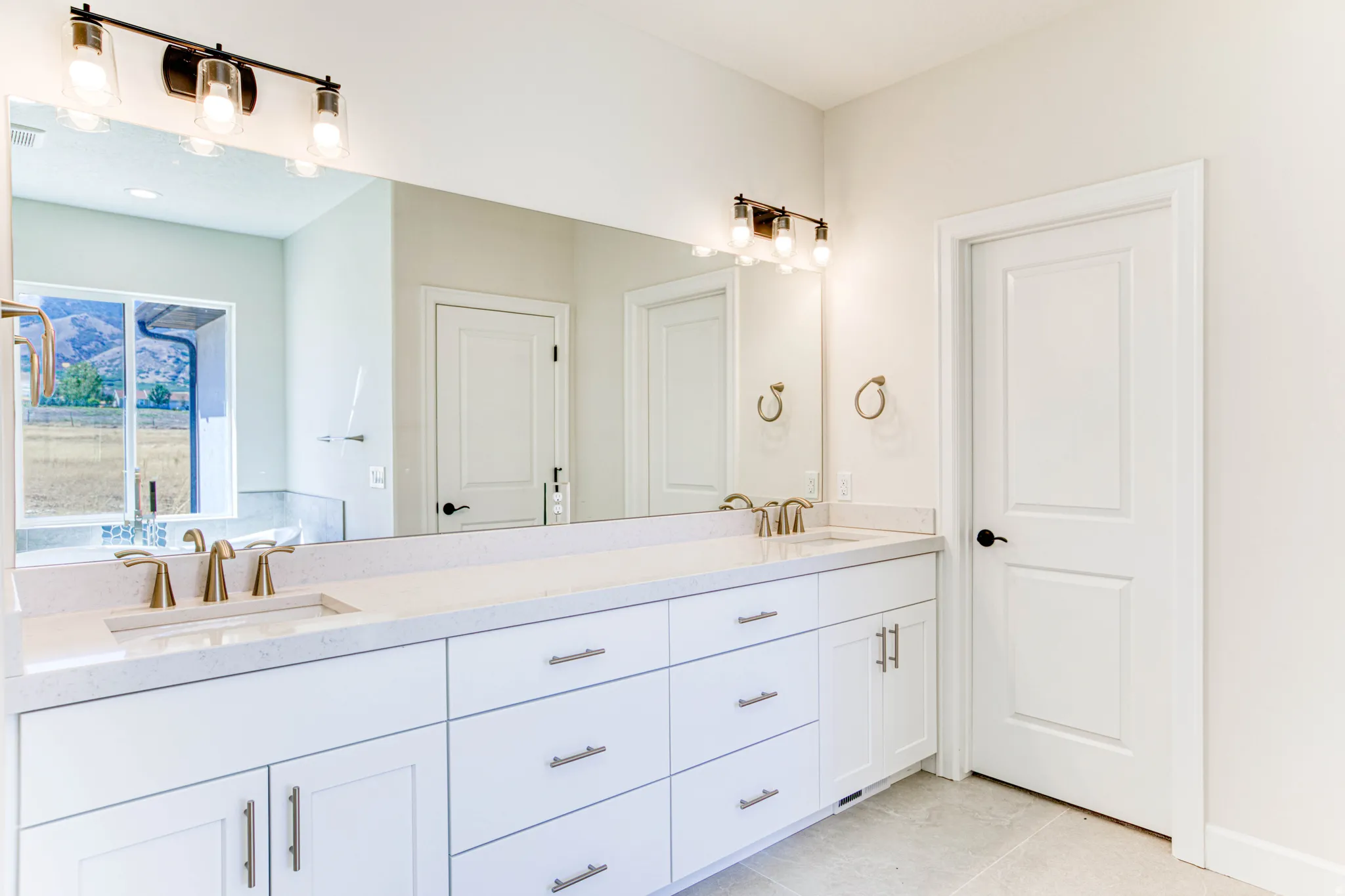 Expansive vanity with dual integrated sinks, brushed gold-finish fixtures, white cabinetry, and a full-width mirror