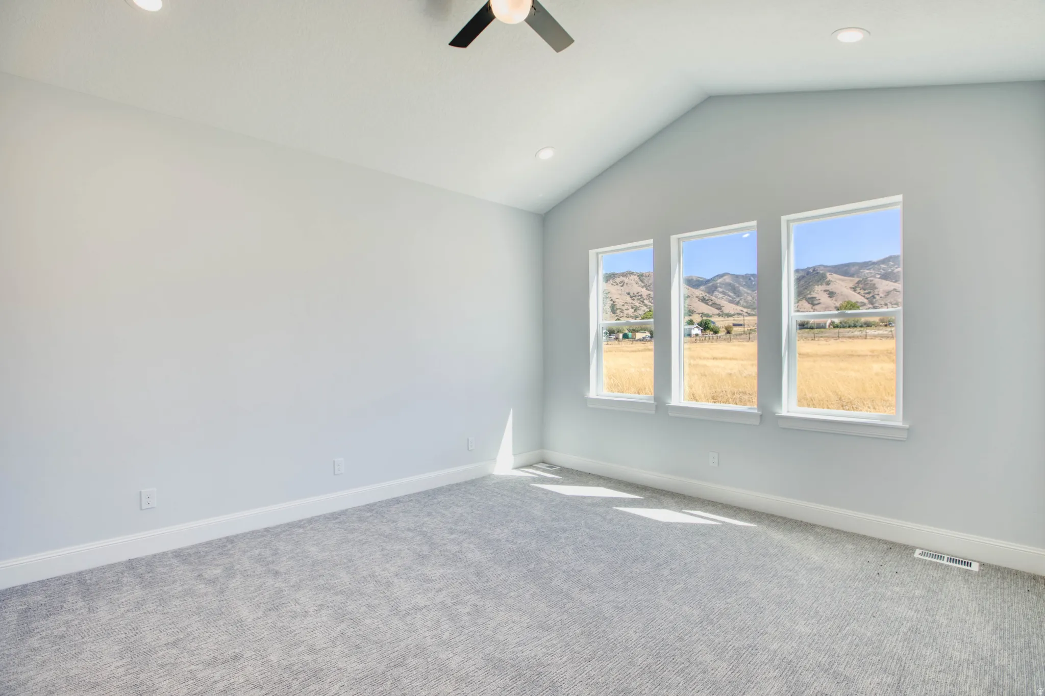 Vaulted ceiling with recessed lighting and ceiling fan, three pane windows, plush carpet flooring, and mountain scenery