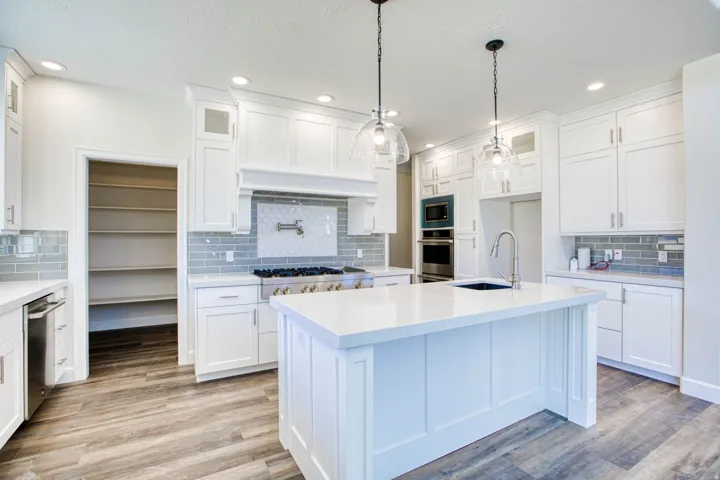 Modern kitchen featuring white cabinetry, light-colored countertops, a tile backsplash, wood-finish flooring, and pendant lighting