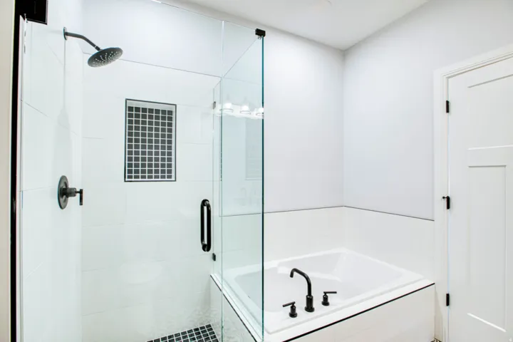 Glass-enclosed shower with matte black fixtures, white subway tile surround, and a recessed niche