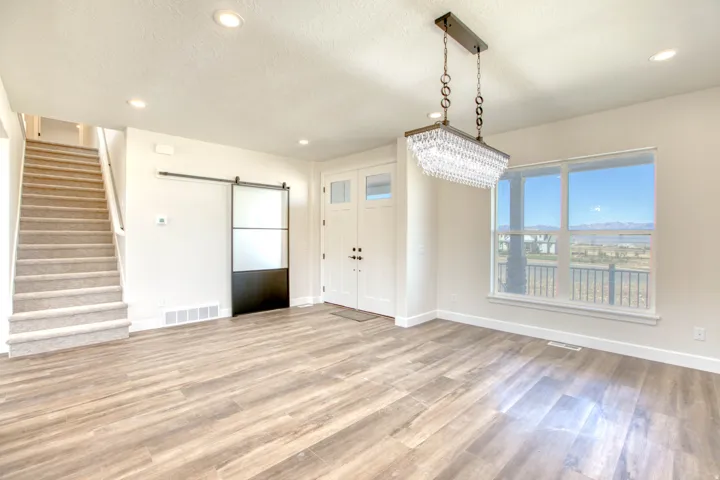 Wood-finish flooring, recessed ceiling lighting, a crystal chandelier, a two-panel front entry door, and an interior barn door