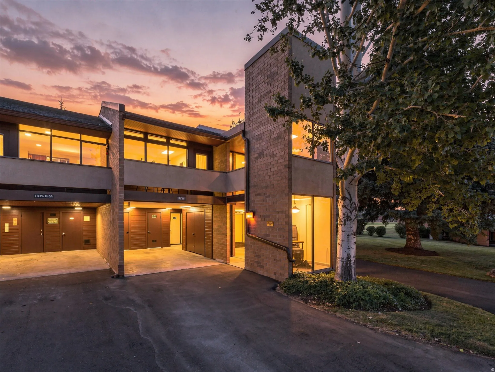 Twilight exterior front view of townhome's carport and entry. Street view, lighting and staircase on right appear digitally altered.
