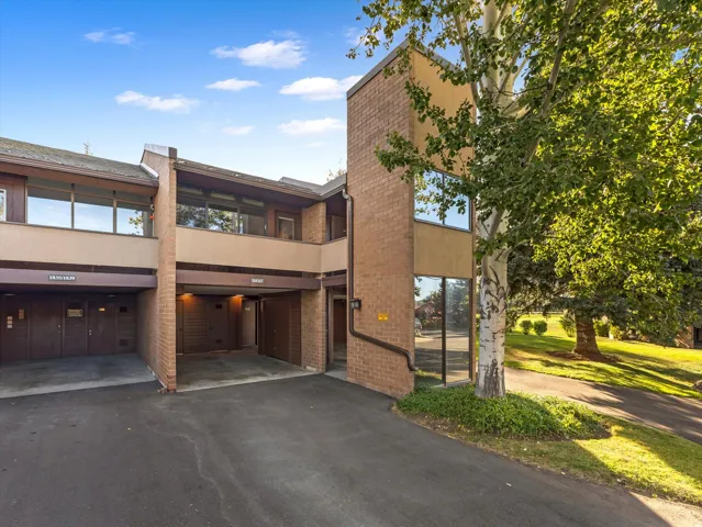 Multi-level architectural design featuring brick accents, large windows, an integrated carport, and mature landscaping