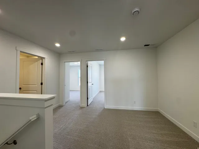 Carpeted landing with recessed lighting, white walls, and multiple doorways