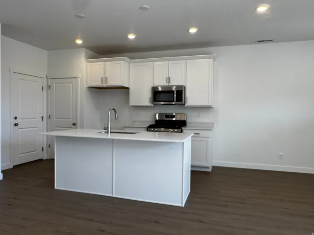 Modern kitchen featuring white cabinetry, stainless steel appliances, a center island with sink, light countertops, and wood-finish flooring