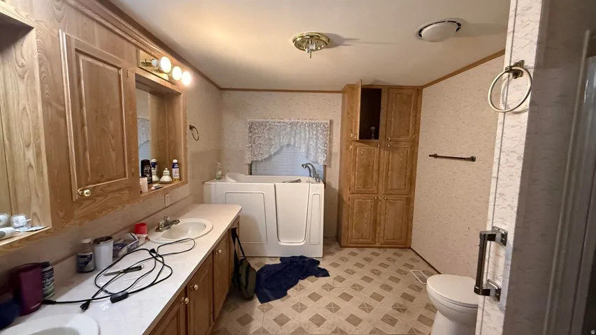 Dual vanity with integrated sinks, walk-in tub, extensive wood-finish cabinetry, and patterned flooring