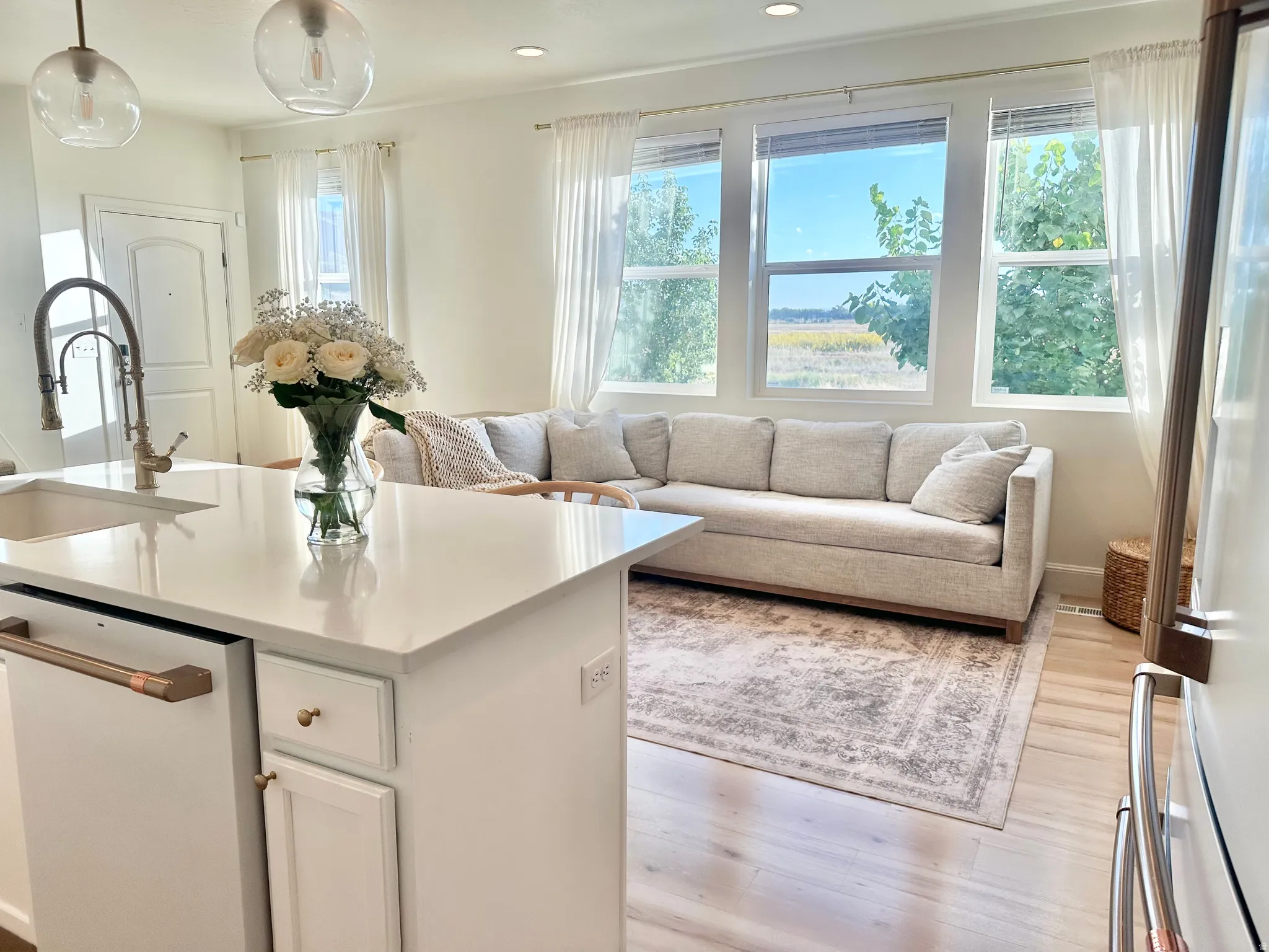 White cabinetry with gold-tone hardware, a white undermount sink with a brass-finish gooseneck faucet, and white countertops