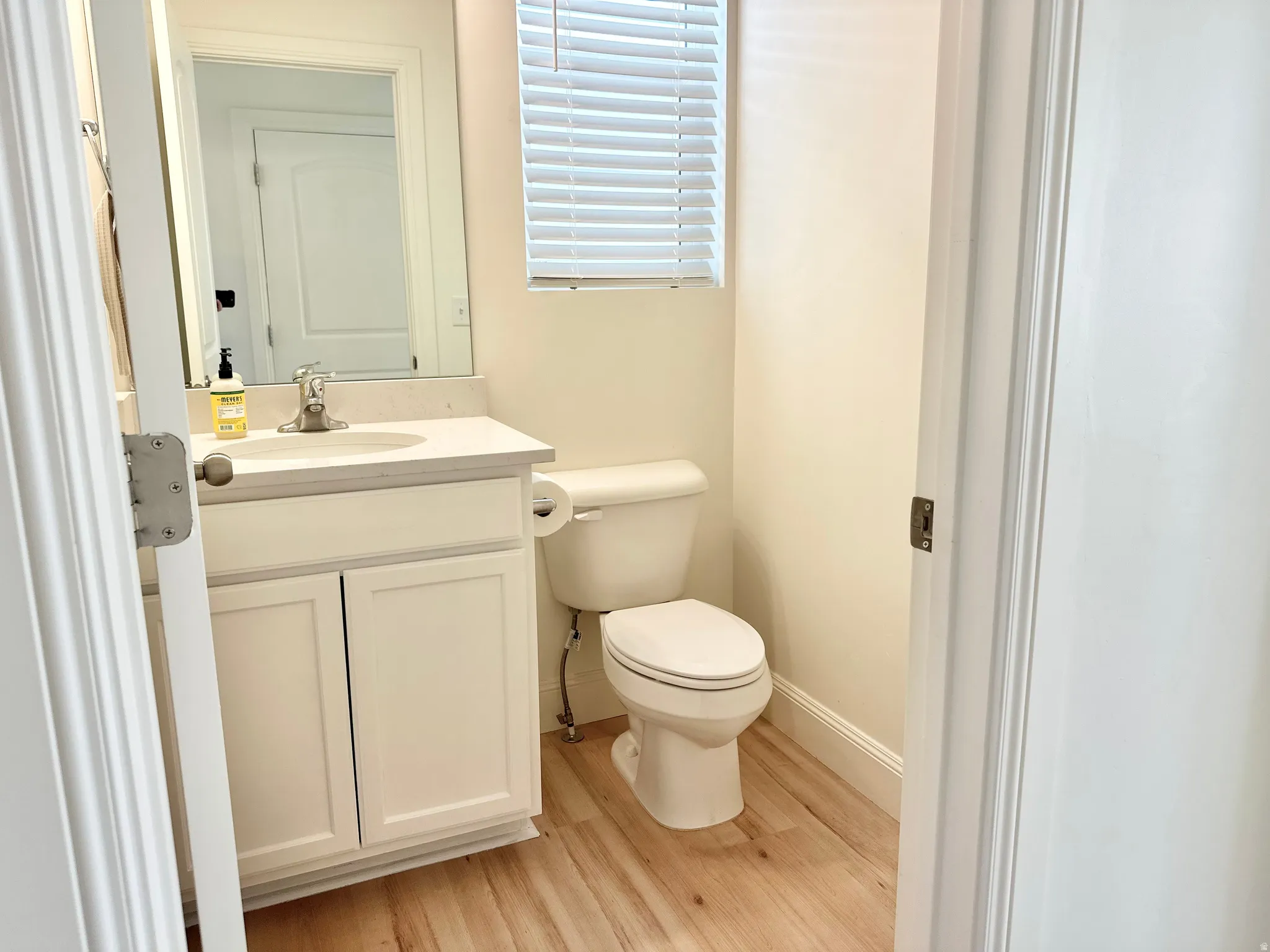 Powder room featuring a single vanity with storage cabinetry, integrated sink, and wood-finish flooring