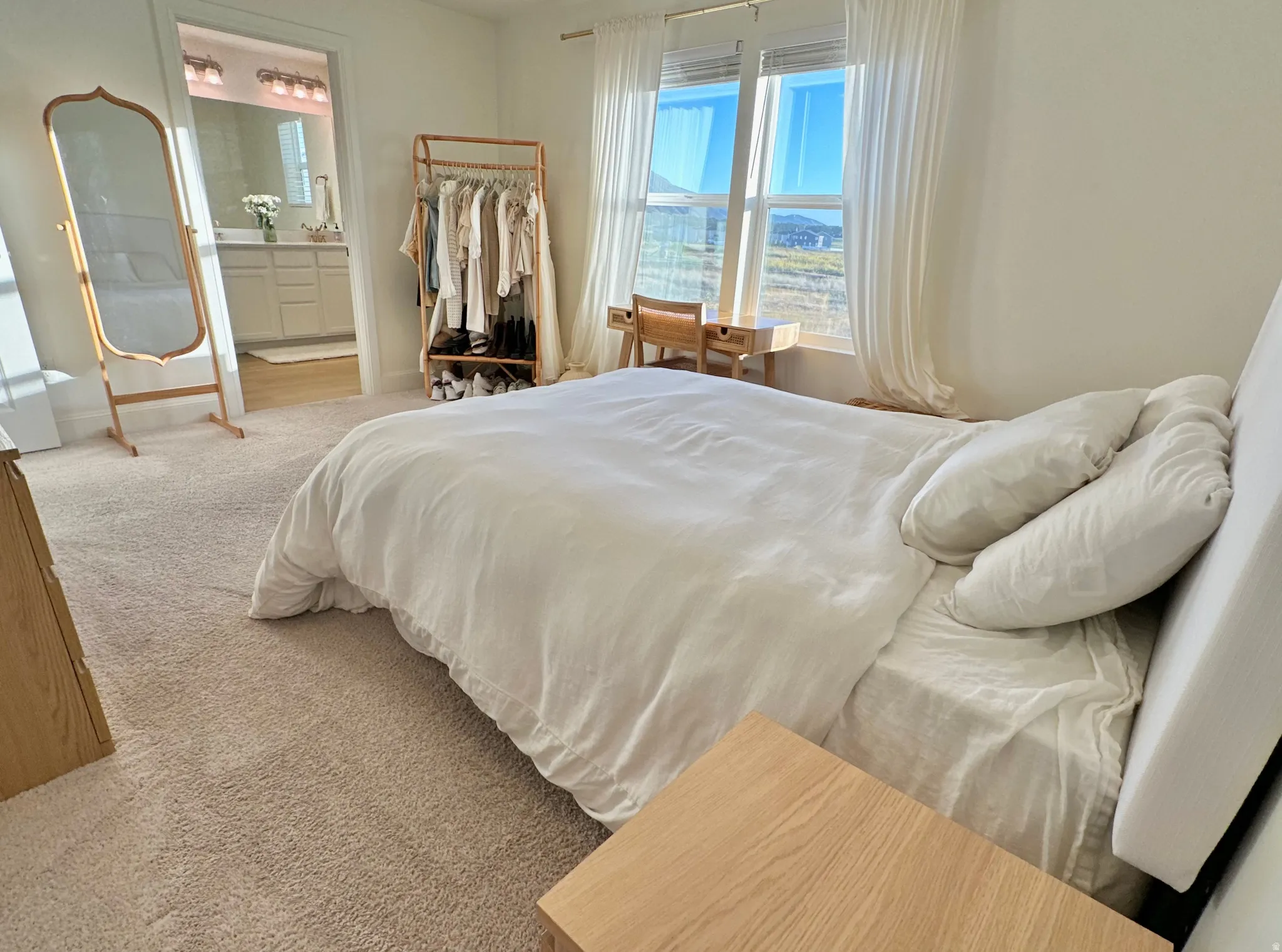 Plush carpet flooring, large windows with white curtains, and a light-colored headboard