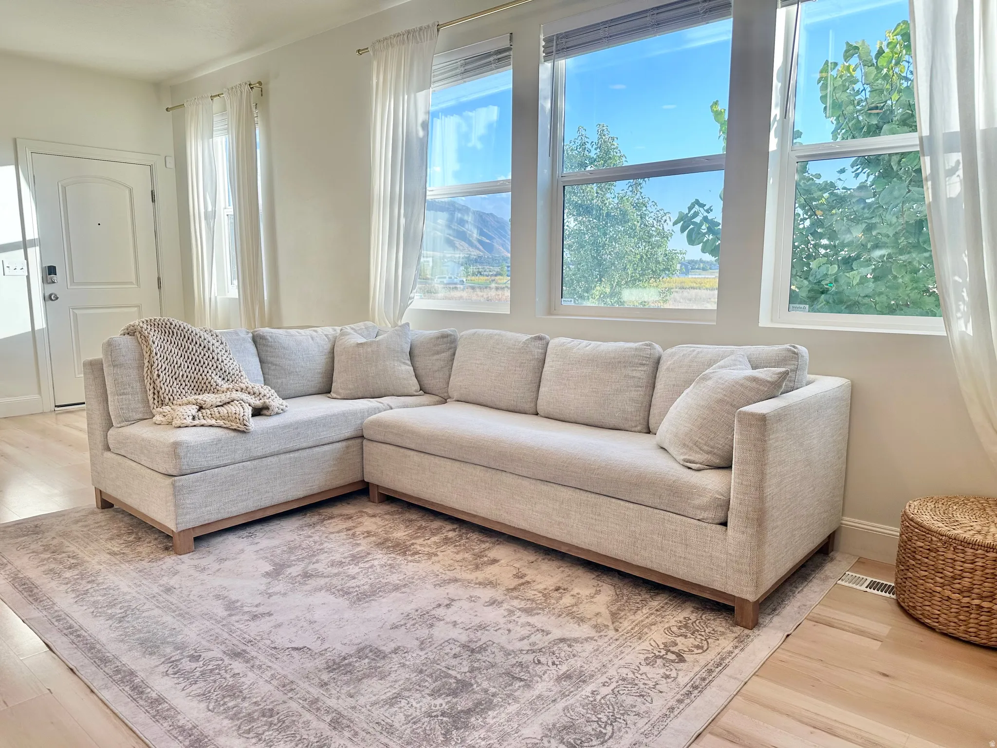 Expansive window bank, light wood-finish flooring, white walls, and a white entry door