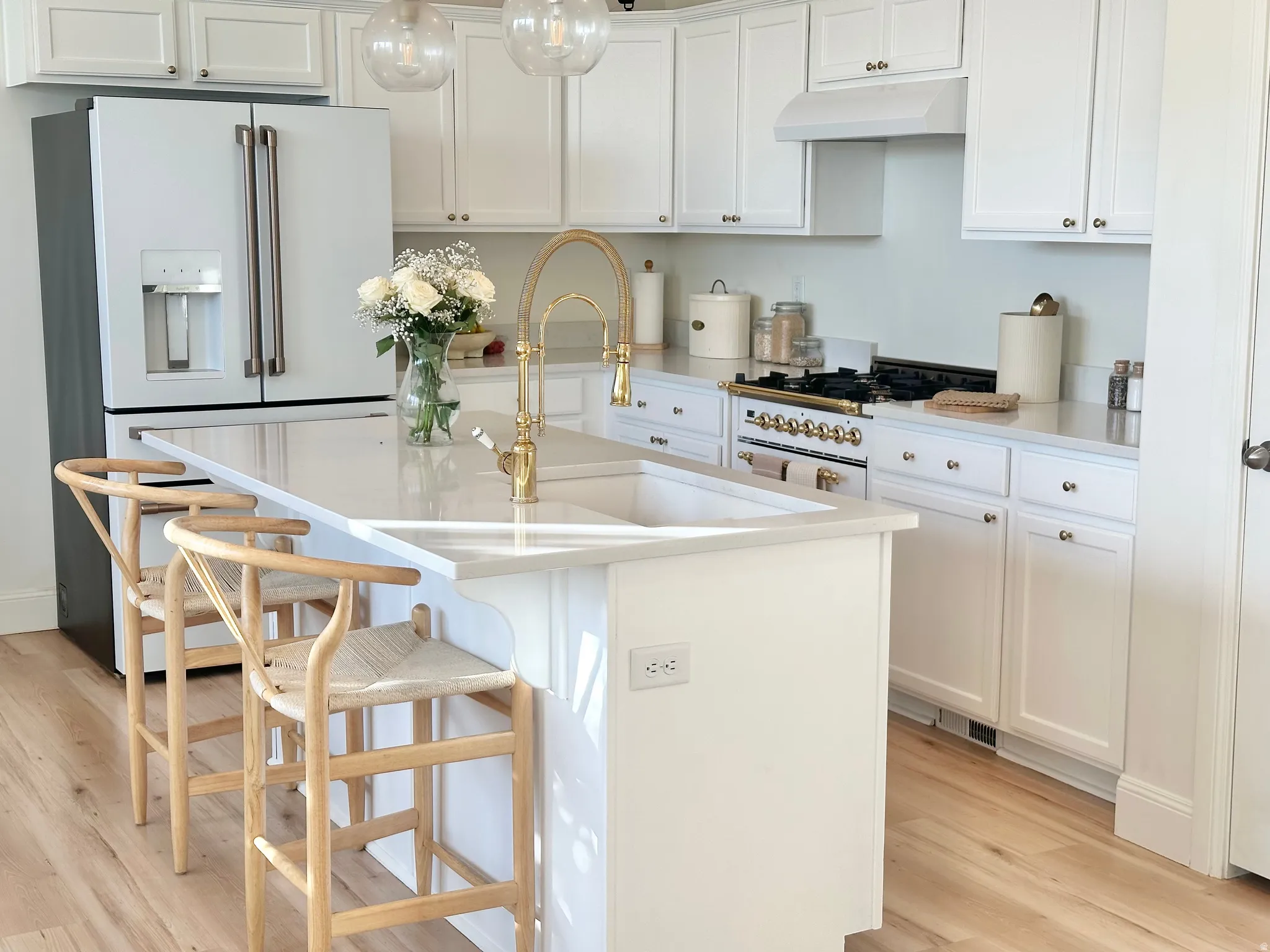 Gourmet kitchen featuring white cabinetry, light countertops, wood-finish flooring, and a central island with an undermount sink