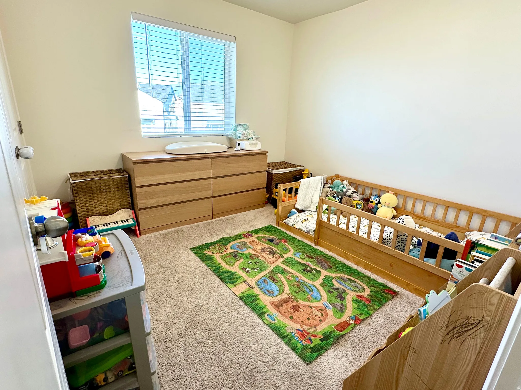 Carpeted room featuring a window with blinds, light-colored walls, and a built-in wood-finish dresser