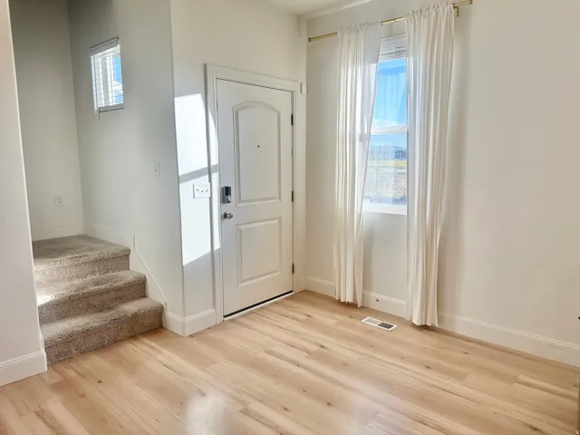 Entryway featuring light wood-finish flooring, a paneled door with smart lock, a carpeted staircase, and an upper window