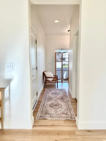Recessed lighting illuminating a hallway with wood-finish flooring and white paneled interior doors