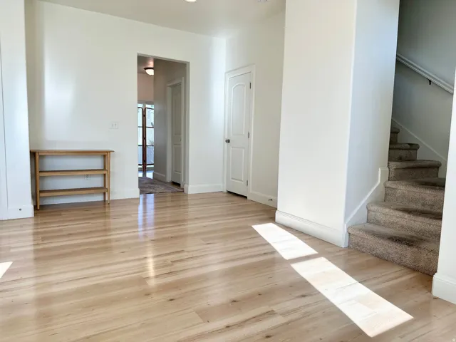 Light wood-finish flooring, white painted walls, and a carpeted staircase with a white handrail