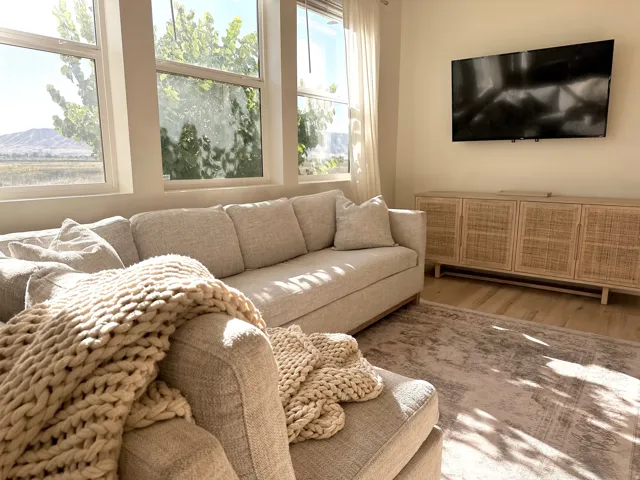 Expansive windows, wood-finish flooring, wall-mounted television, and a built-in media console with woven door fronts