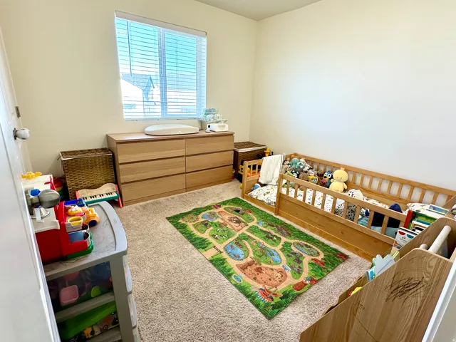 Carpeted room featuring a window with blinds, light-colored walls, and a built-in wood-finish dresser