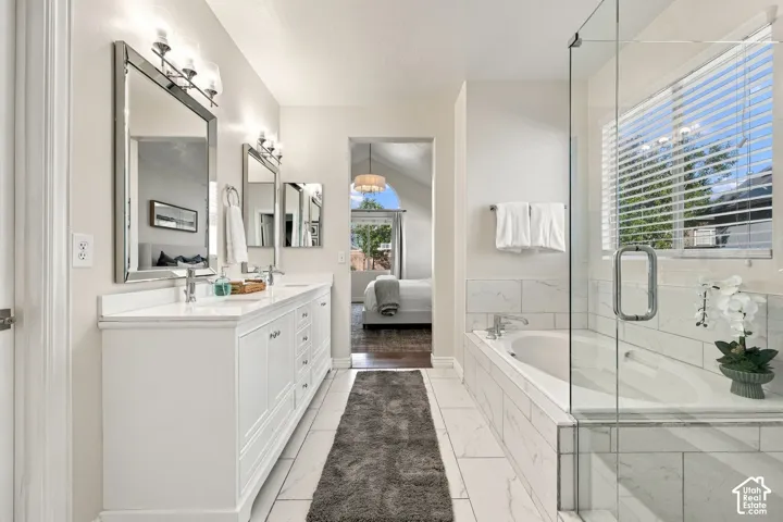 Dual vanity with white cabinetry and chrome fixtures, large soaking tub, separate glass-enclosed shower, polished tile flooring, and wall-mounted vanity lighting