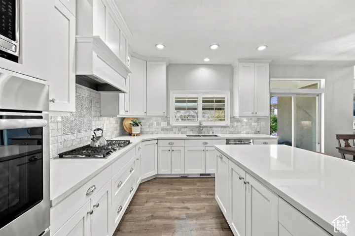 Kitchen with white cabinetry, light-toned countertops, tile backsplash, wood-finish flooring, and recessed lighting