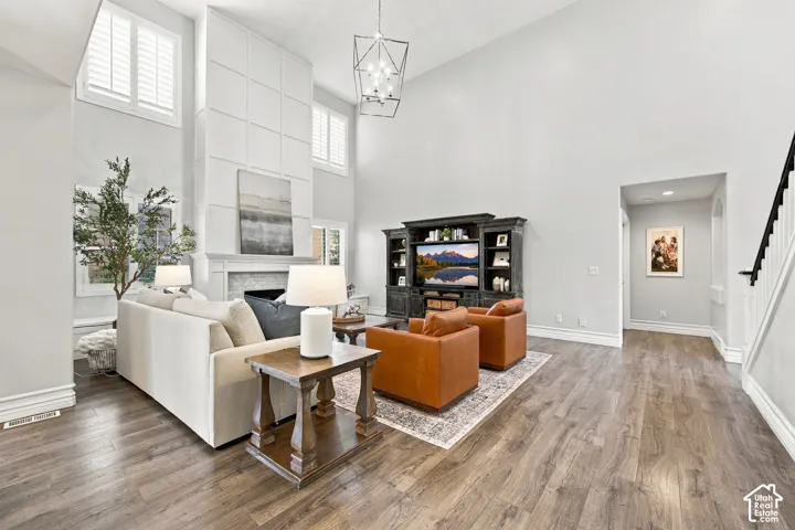 Vaulted ceiling with a geometric chandelier, fireplace with a decorative mantel, wood-finish flooring, and a staircase with a black handrail