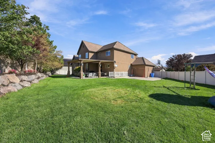 Expansive lawn with a stone retaining wall, mature trees, a covered patio, and a privacy fence