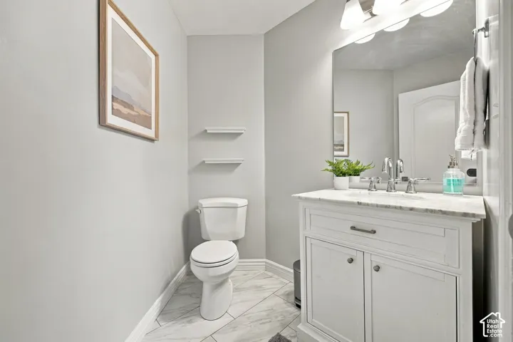 White vanity with a stone countertop, chrome fixtures, and a frameless mirror