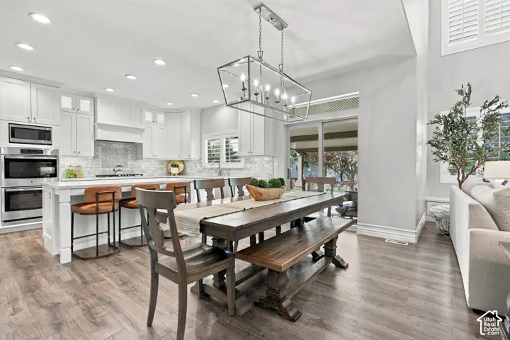 Wood-finish flooring, white cabinetry, stainless steel appliances, sliding glass doors, and a decorative chandelier