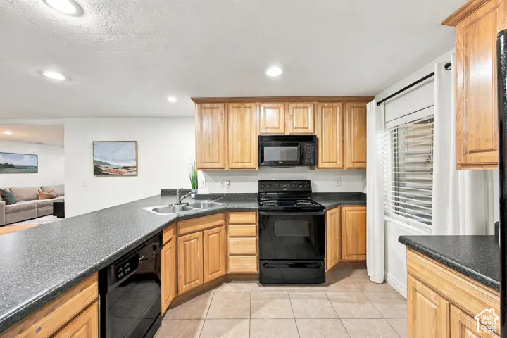 Kitchen with wood cabinetry, black appliances, tile flooring, and dark countertops
