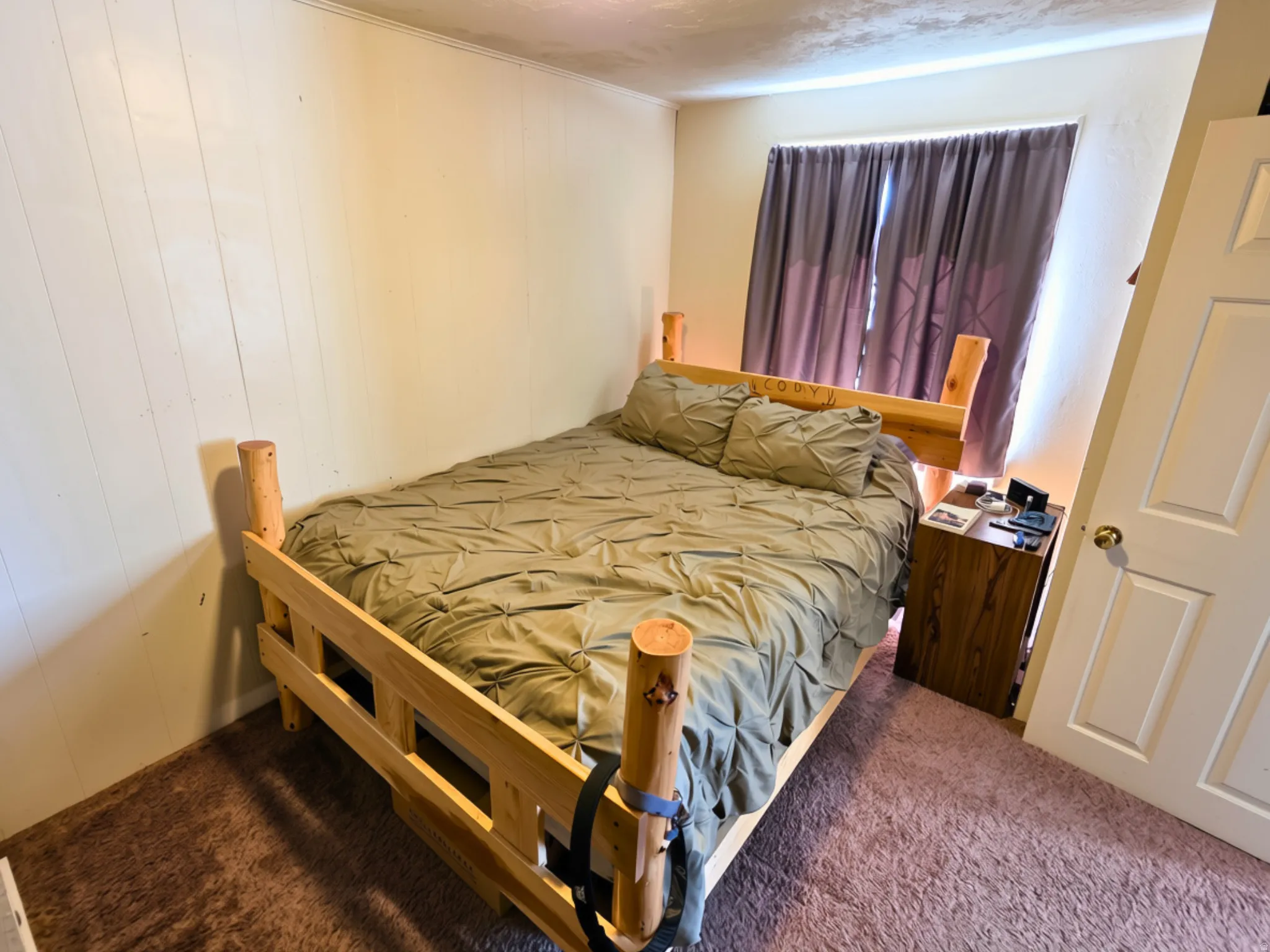 Carpeted flooring, paneled wall finishes, and a single window with curtain rods