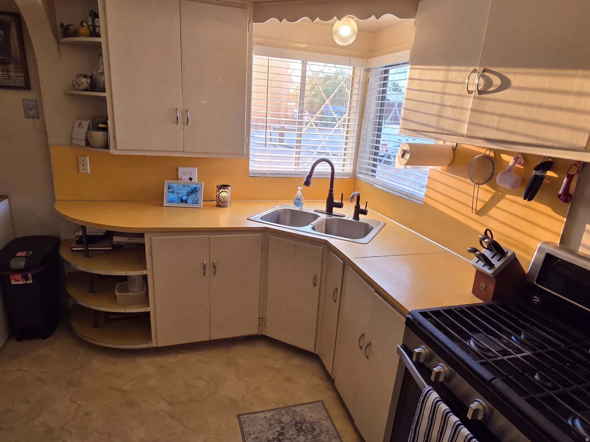Corner kitchen sink with dual basins, a modern faucet, and a large window with blinds