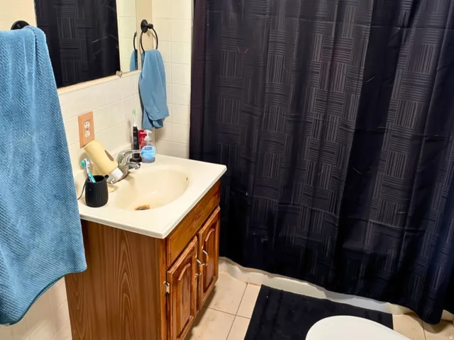 Vanity with wood-finish cabinetry and integrated sink, ceramic tile flooring, and tiled shower surround
