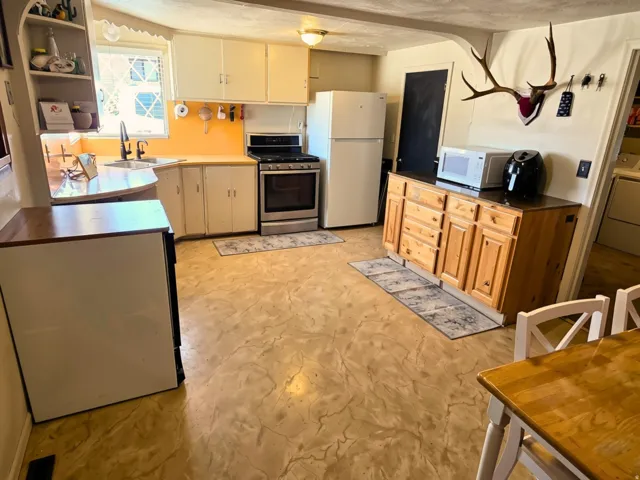 Kitchen featuring light-toned cabinetry, a stainless steel range, a built-in corner shelf, a window above the sink, and patterned flooring