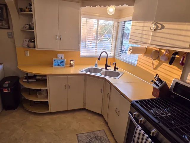 Corner kitchen sink with dual basins, a modern faucet, and a large window with blinds