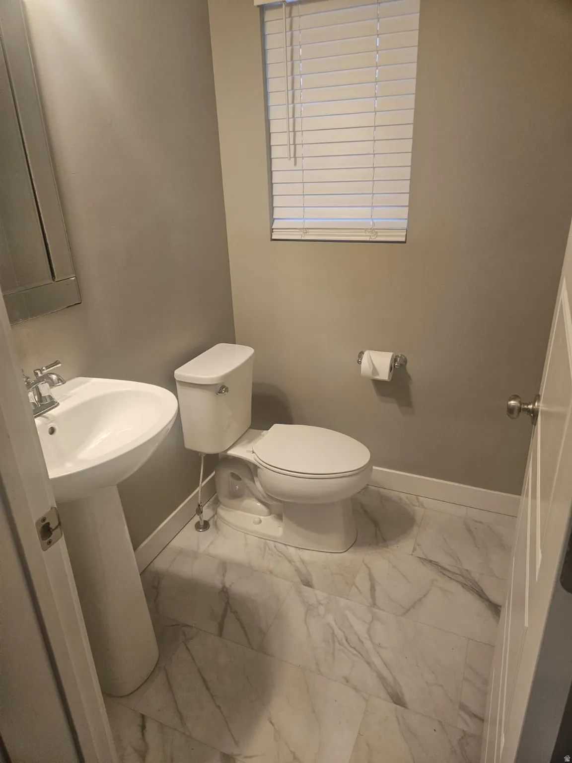 Pedestal sink, window with blinds, and white toilet