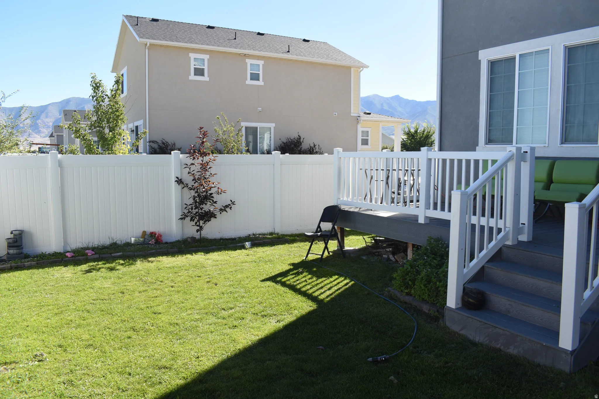 Manicured lawn with a white vinyl fence, multi-level deck featuring white railings, and sliding glass doors
