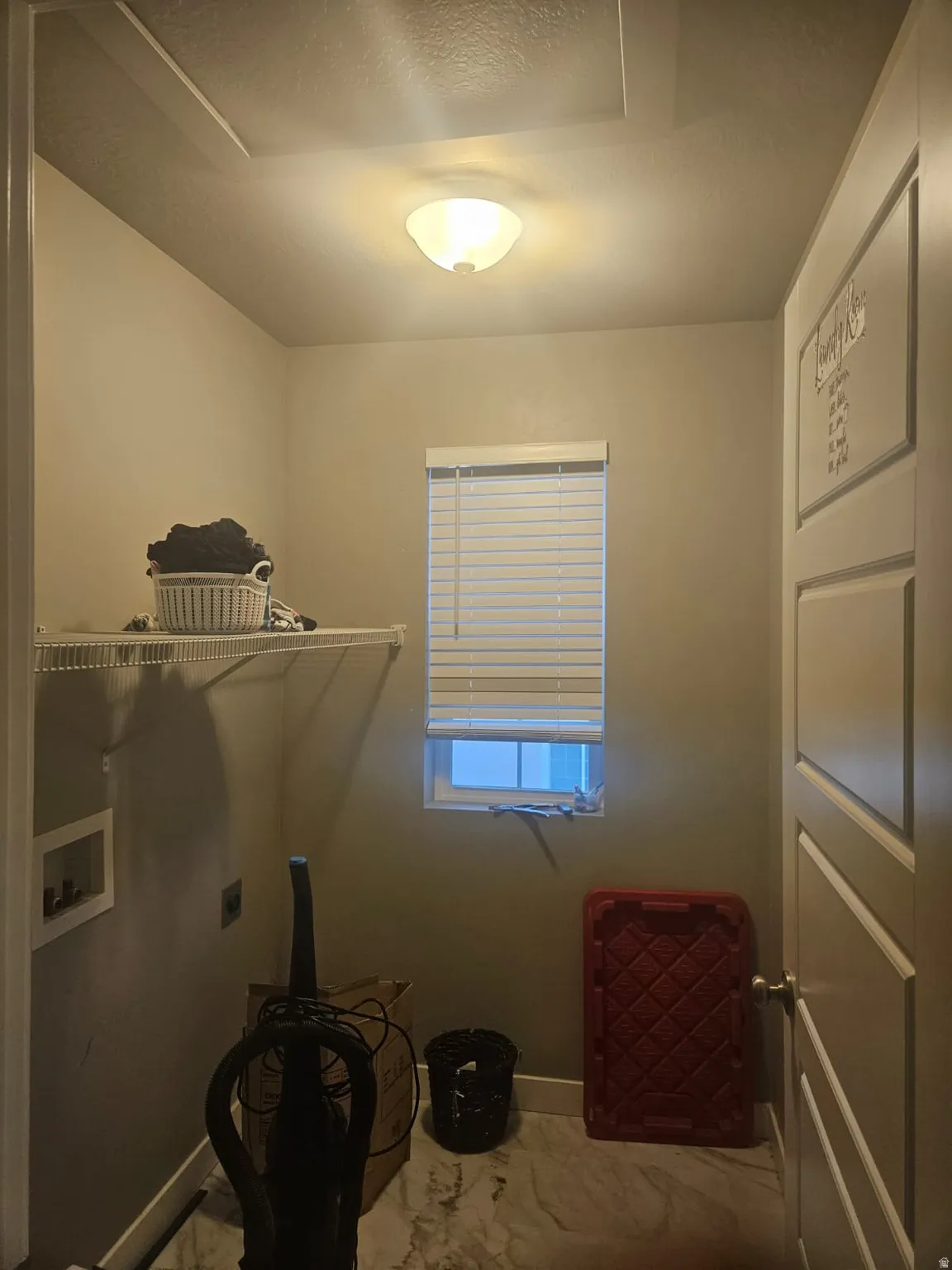 Recessed wall box with hookups, single window with blinds, overhead lighting fixture, and wire shelving