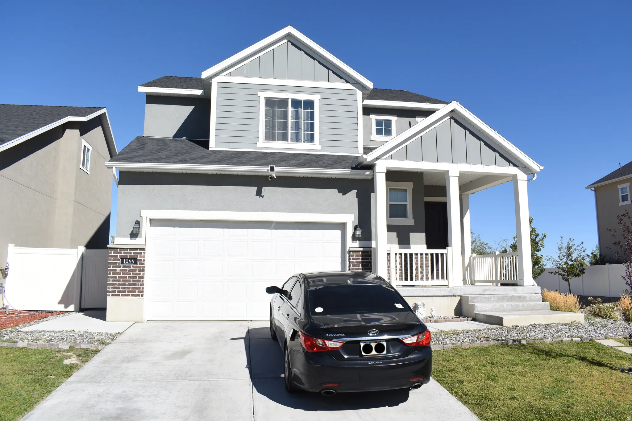 Two-story residence with a covered front porch featuring white columns and railing, a two-car garage, and gray siding accents
