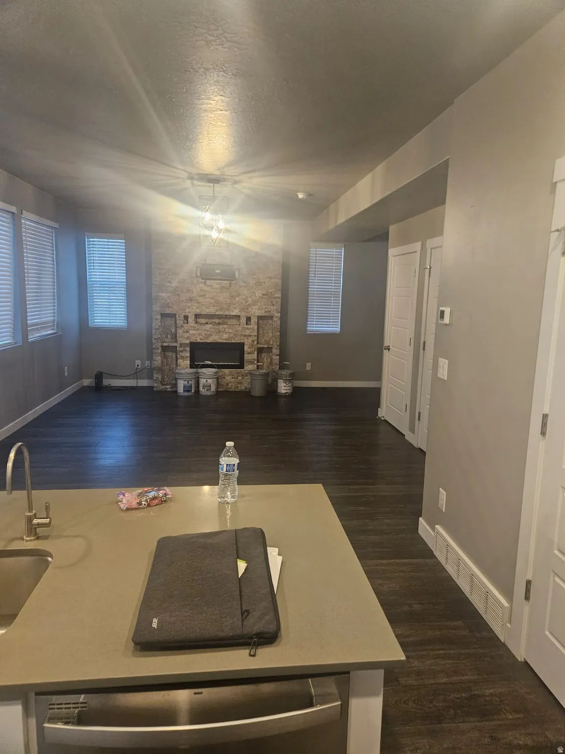Open-concept living space with dark wood-finish flooring, a stone-clad fireplace, and multiple windows with blinds