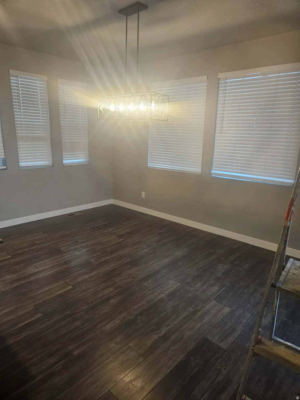 Wood-finish flooring complemented by multiple windows with blinds and a contemporary linear chandelier