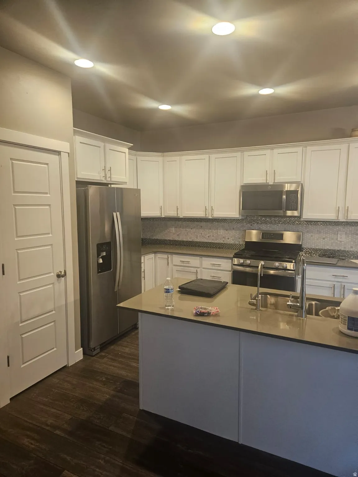 Kitchen featuring white cabinetry, stainless steel appliances, a center island with sink, mosaic tile backsplash, and wood-finish flooring