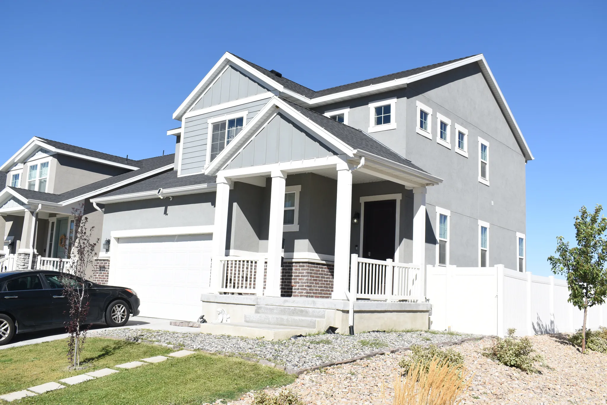 Gray stucco exterior with white trim, covered front porch, integrated two-car garage, and a white privacy fence