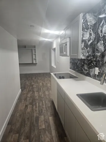 Wood-finish flooring, white cabinetry, integrated cooktop, stainless steel sink, and a dark patterned backsplash
