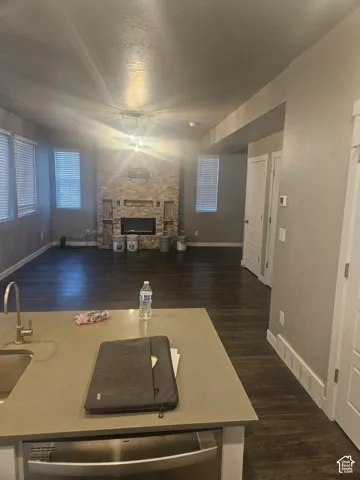 Open-concept living space with dark wood-finish flooring, a stone-clad fireplace, and multiple windows with blinds