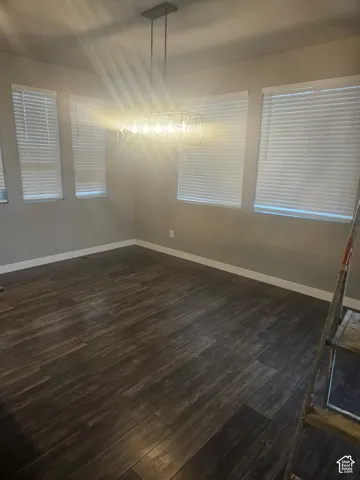 Wood-finish flooring complemented by multiple windows with blinds and a contemporary linear chandelier