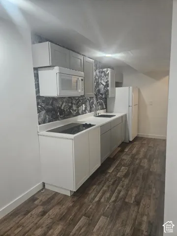 Kitchenette with wood-finish flooring, white cabinetry, integrated cooktop, and a stainless steel over-the-range microwave