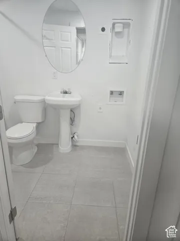Pedestal sink with chrome faucet, toilet, wall-mounted oval mirror, and tile flooring