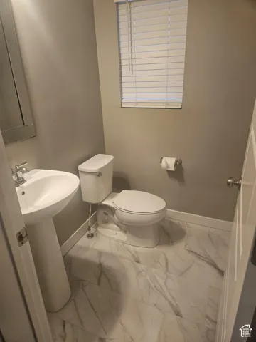 Pedestal sink, window with blinds, and white toilet